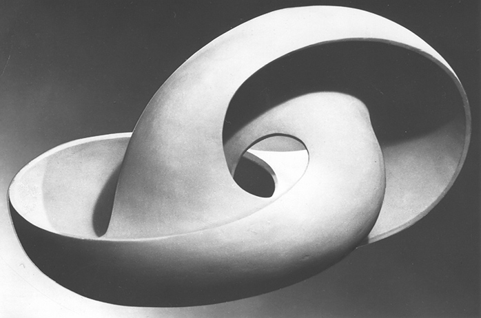 Abstrakcyjna rzeźba o gładkich, obłych kształtach, przypominająca skręconą wstęgę lub muszlę. Wykonana z jasnego materiału, z otworem w centrum. Minimalistyczna forma na ciemnym tle.